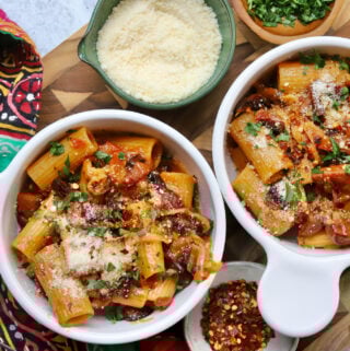 Rigatoni Pasta in white bowls with parmesan, parsley, and red pepper flakes.